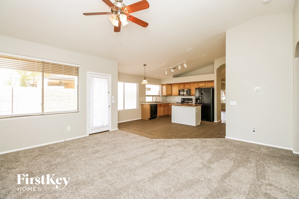 an empty living room with a ceiling fan and a kitchen