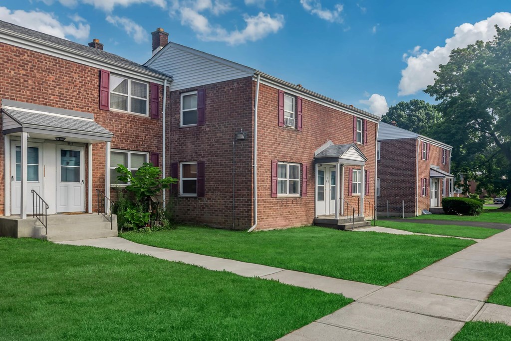 a brick apartment building with green grass and a sidewalk
