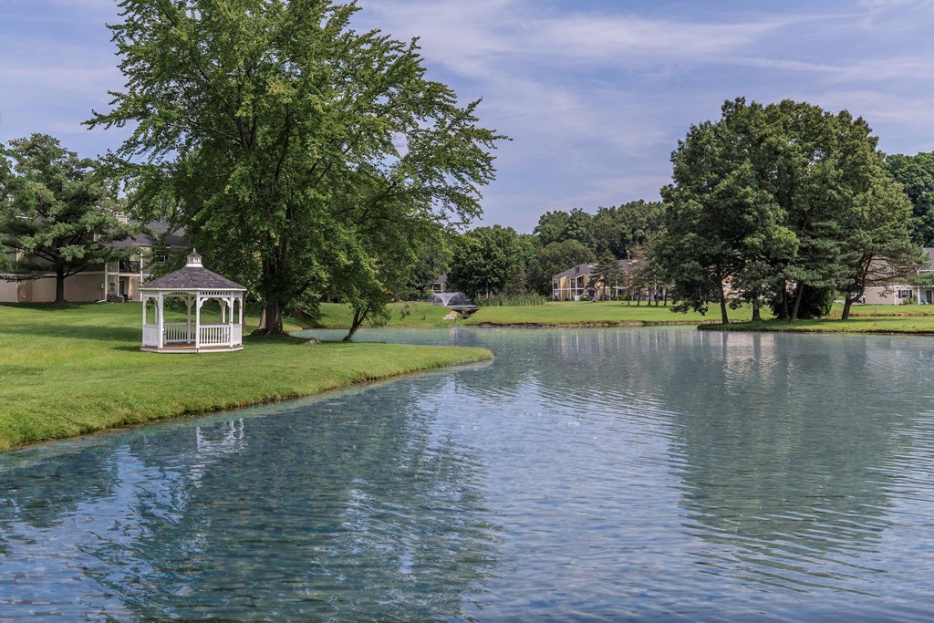 a gazebo sits on the grass next to a pond