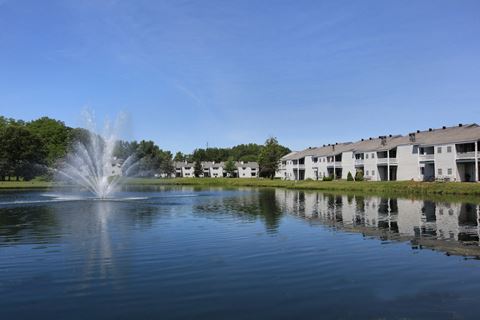 a fountain in the pond with apartment buildings in the background