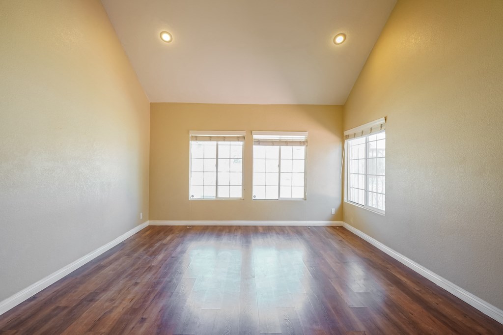 an empty living room with wood flooring and two windows