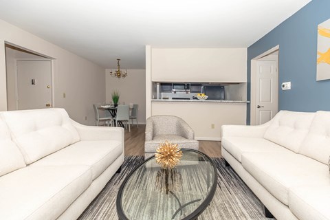 A living room with a glass coffee table and two white couches.