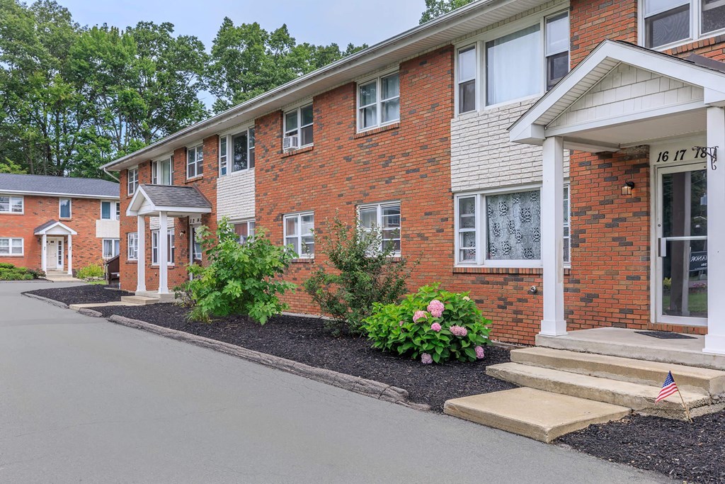 the front of a brick apartment building with steps and landscaping