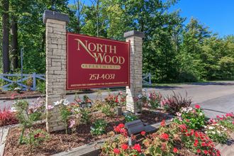 a sign for north wood at the entrance of a park with flowers