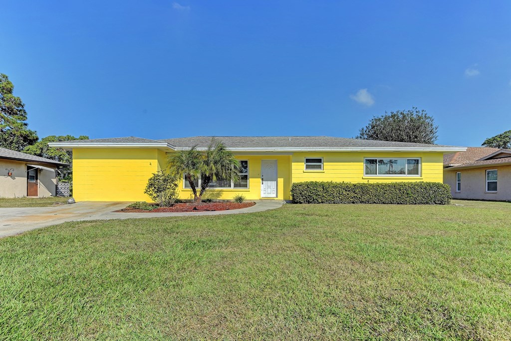 A yellow building with a grey roof and a green lawn in front.