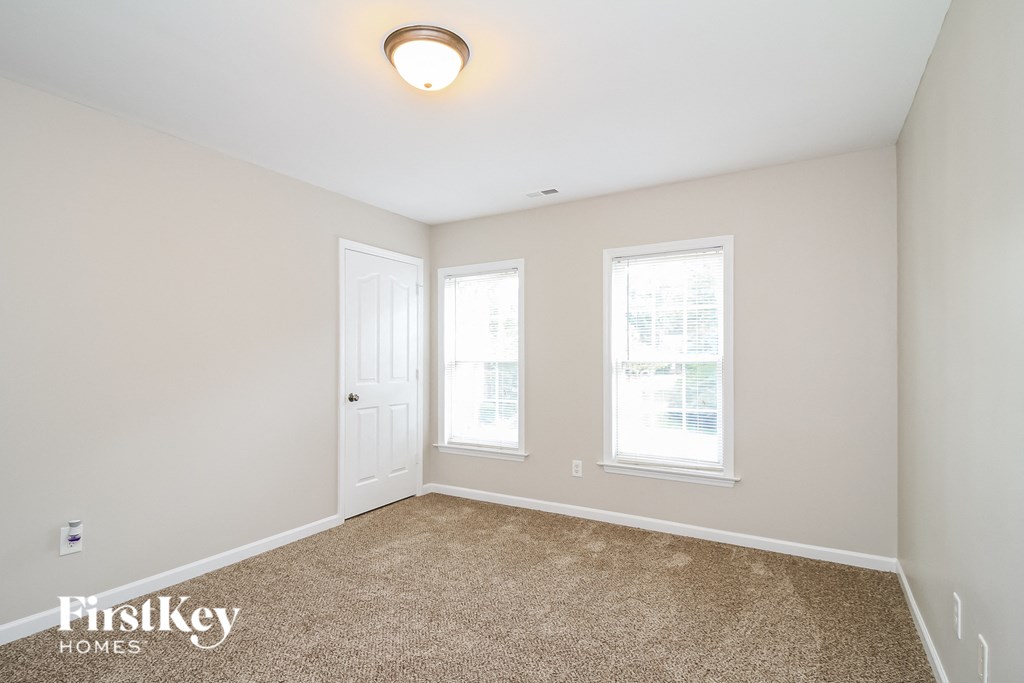 A room with a carpeted floor and two windows.