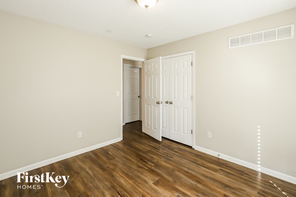 a bedroom with white walls and wood flooring and a closet