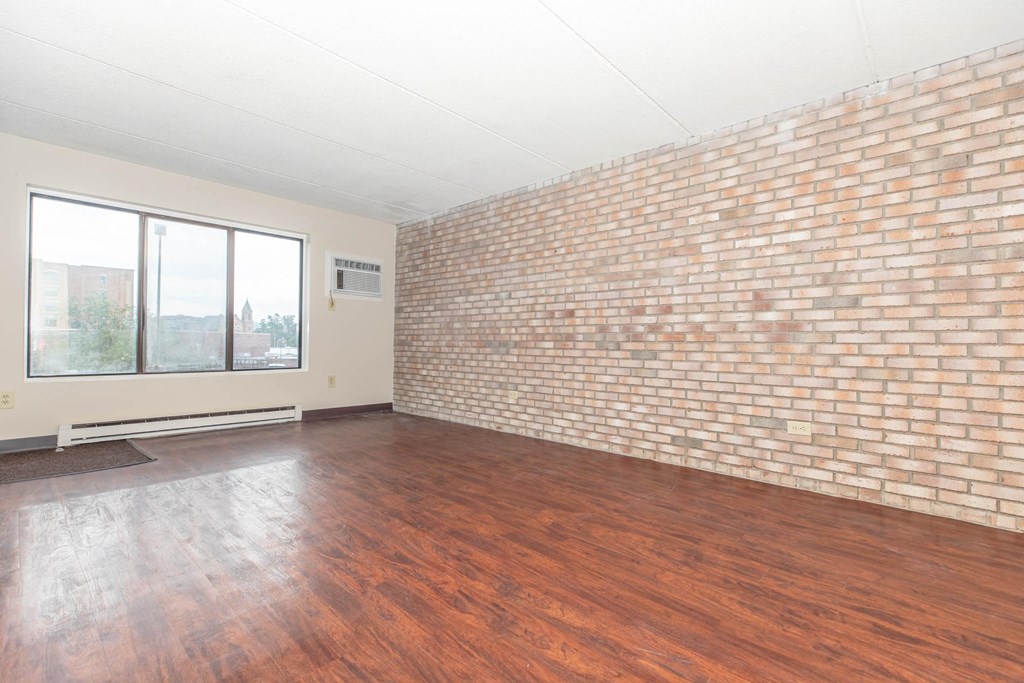 an empty living room with a brick wall and wood floors