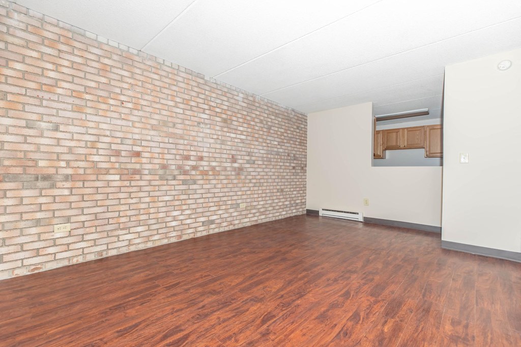 an empty living room with wood floors and a brick wall