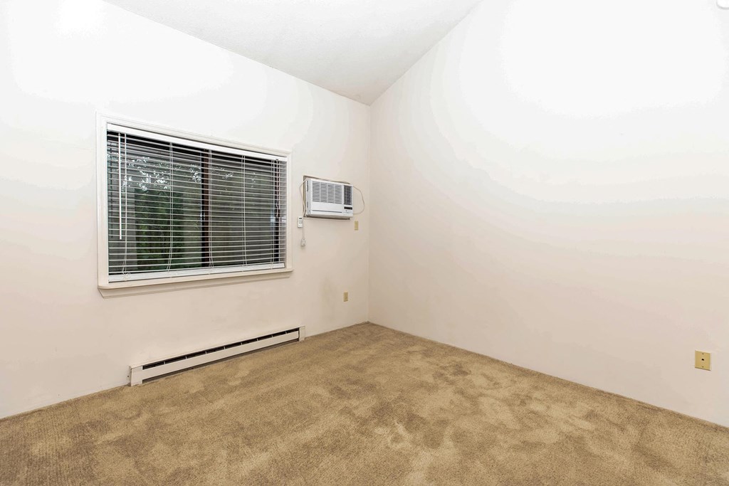 a room with a window and carpet and a heater on the wall