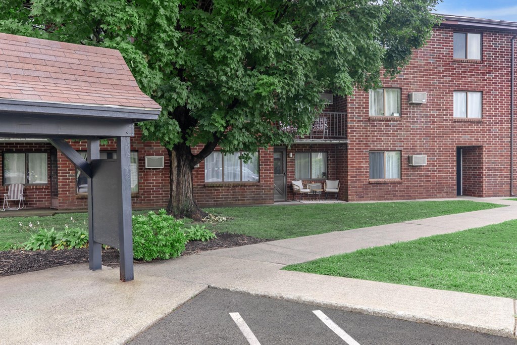 a sidewalk in front of a brick building with a tree