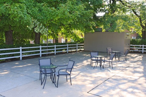 a patio with tables and chairs in the shade of trees