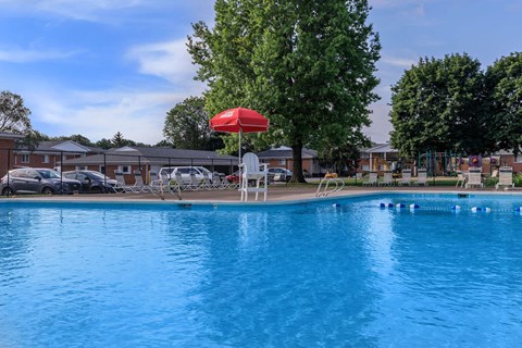 a swimming pool with a red umbrella and chairs around it