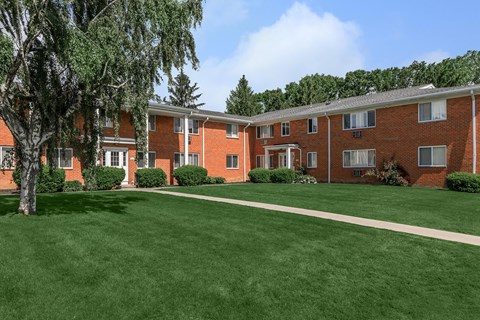 exterior view of a brick apartment building with green grass and trees