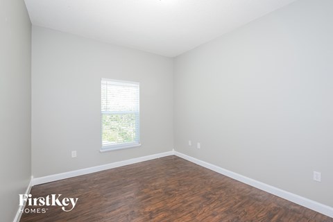 a bedroom with white walls and wood flooring and a window