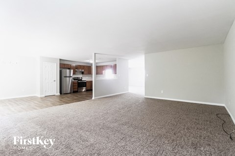 A carpeted room with a kitchen in the background.