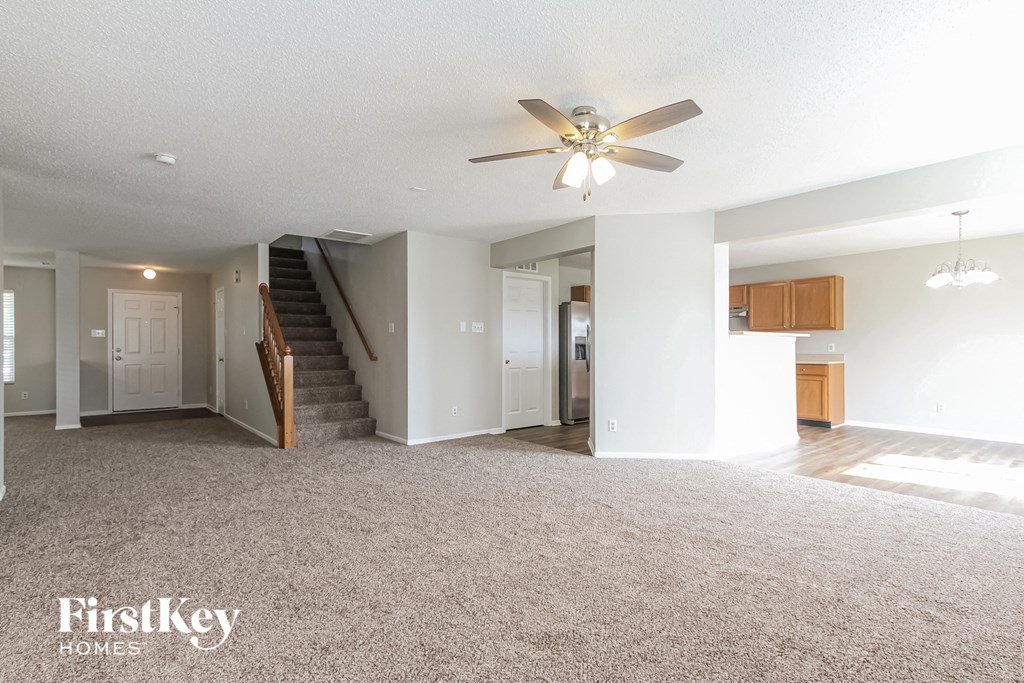 an empty living room with a ceiling fan and a kitchen
