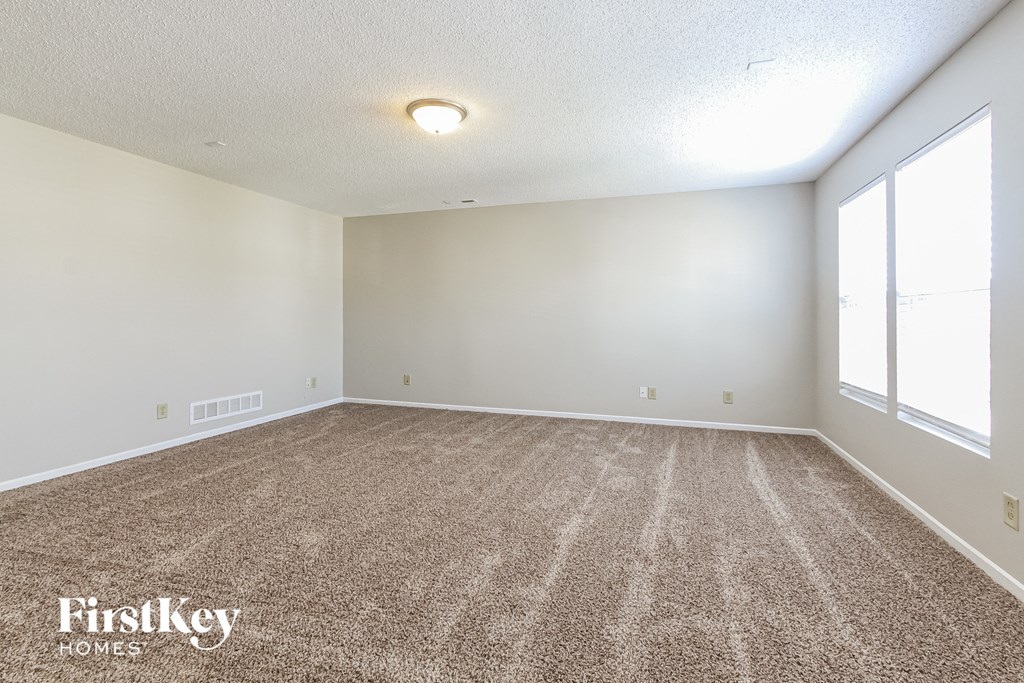 a spacious living room with carpet and large windows