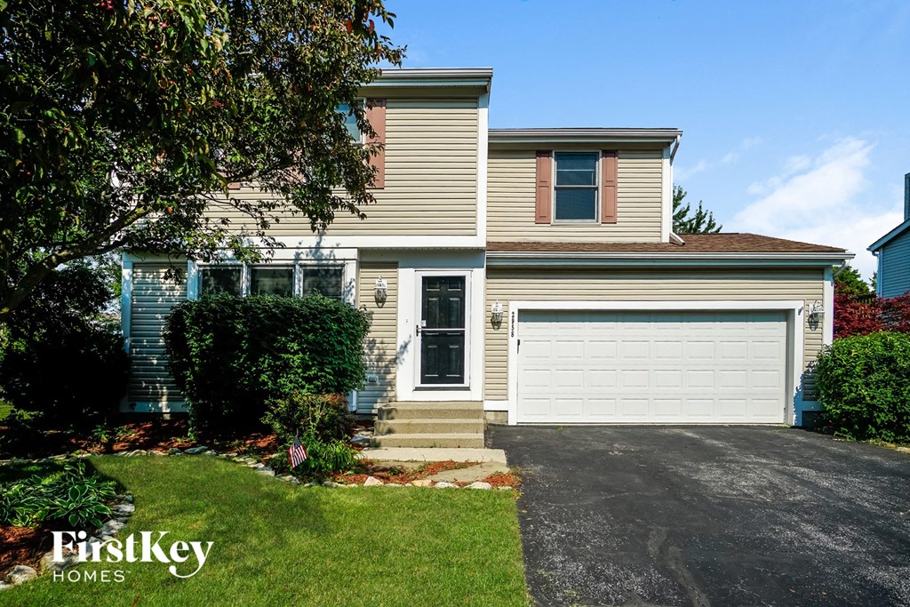 A house with a garage door and a tree in front of it.