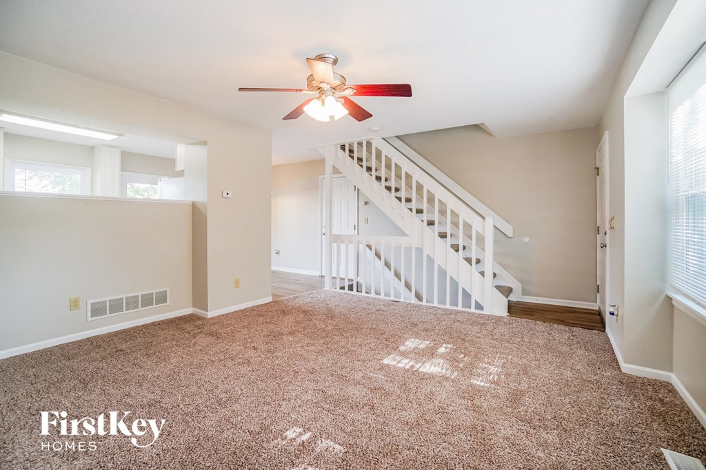 A carpeted room with a staircase and a ceiling fan.