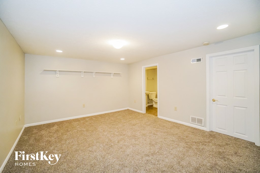 A spacious room with a carpeted floor and white walls, with a doorway leading to another room.