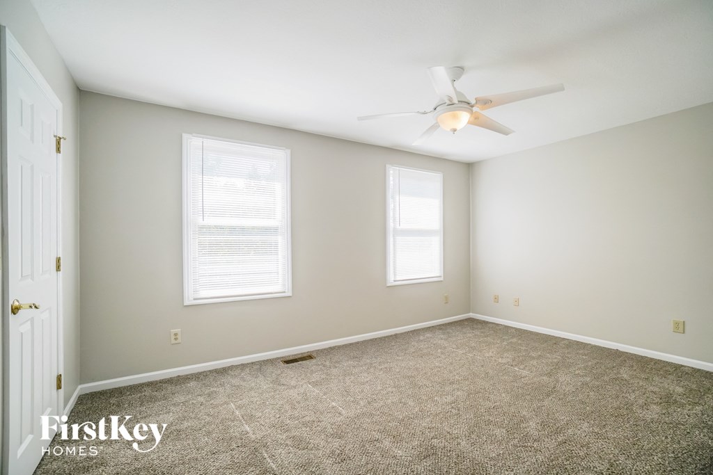 A spacious room with a ceiling fan and two windows.