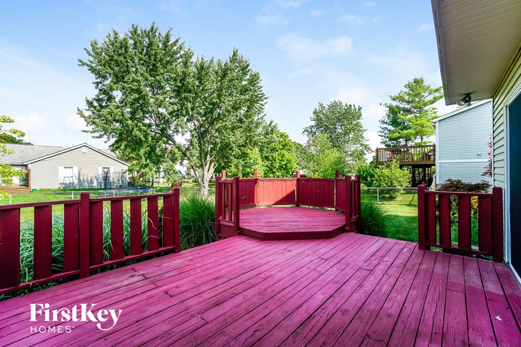 A wooden deck with a red railing and a tree in the background.