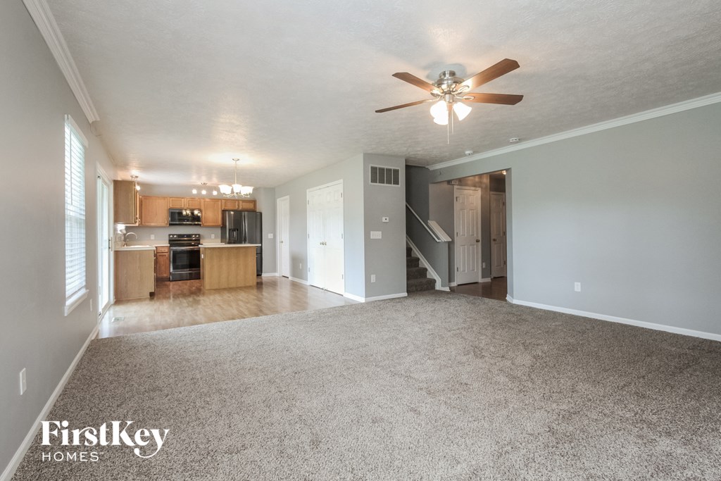 an empty living room with a ceiling fan and a kitchen