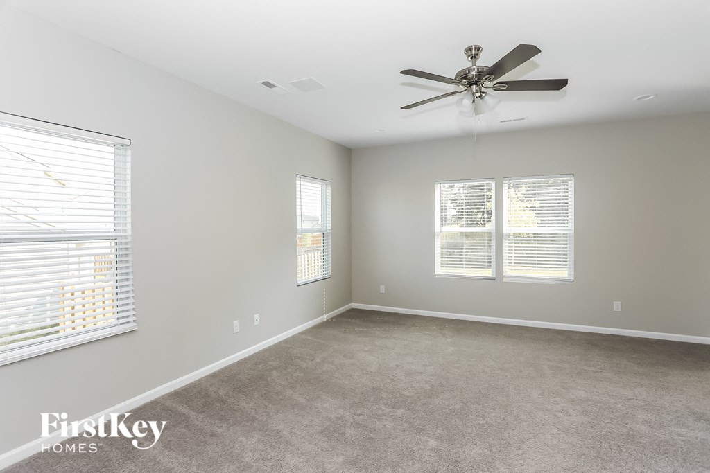 an empty living room with a ceiling fan and two windows