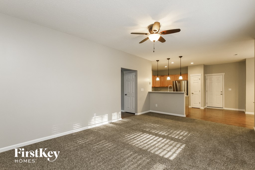 an empty living room with a ceiling fan and a kitchen