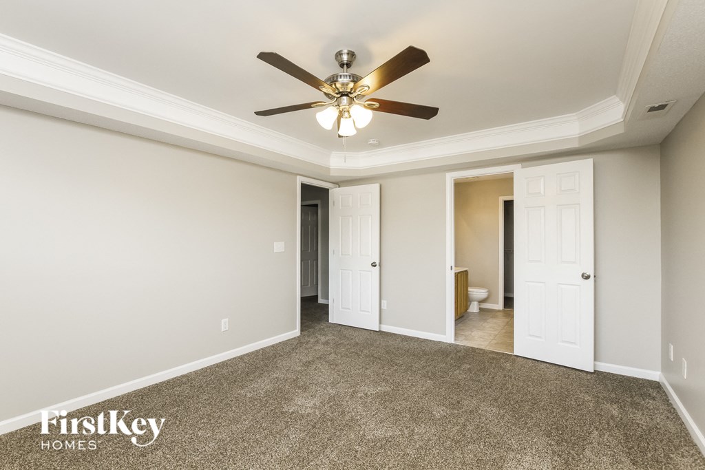 an empty living room with a ceiling fan and a door to a bathroom