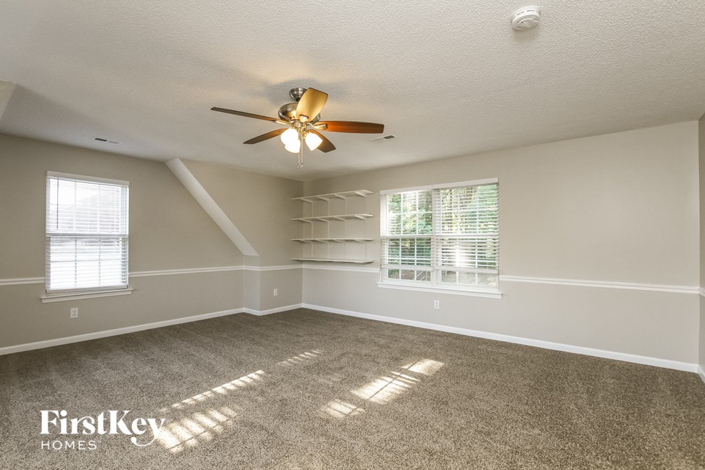 an empty living room with a ceiling fan and shelves