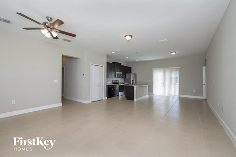 A spacious room with a ceiling fan and a kitchenette in the background.