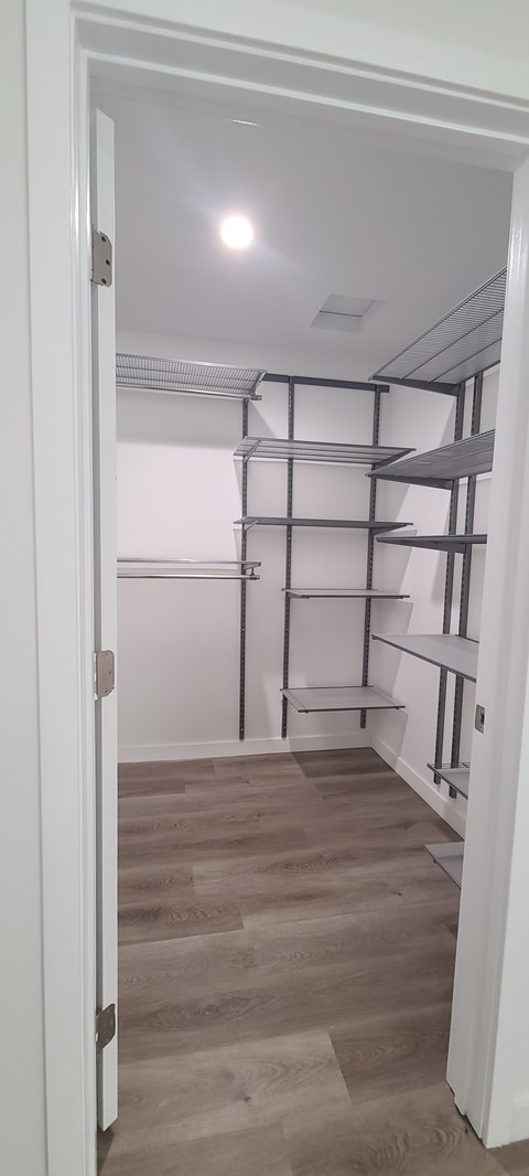 A white door is open to a room with a white ceiling and a wall with shelves.