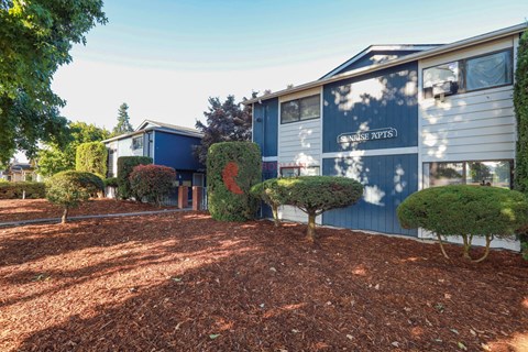 A blue building with the words "CARNISSE APIS" on it is surrounded by trees and shrubs.