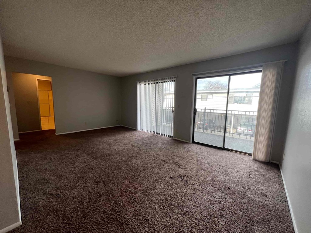 an empty living room with large windows and a carpet