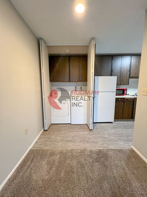 A carpeted room with a white refrigerator and wooden cabinets.