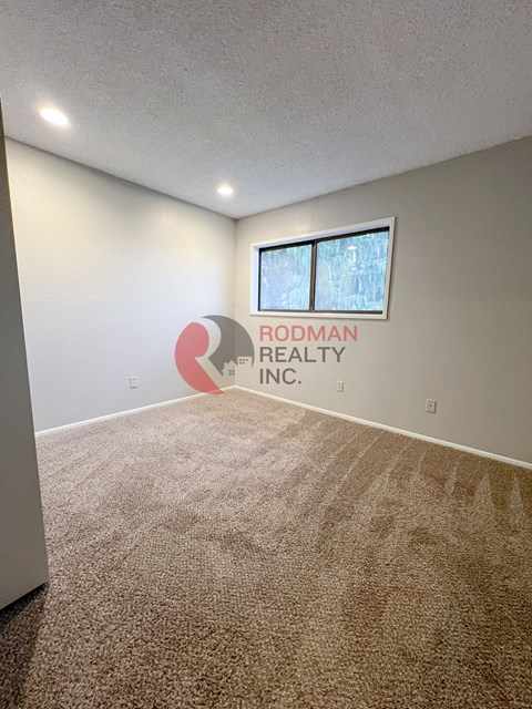 A carpeted room with a window and a sign that says Rodman Realty Inc.