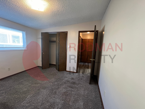 A room with a carpeted floor and two doors, one of which is open.