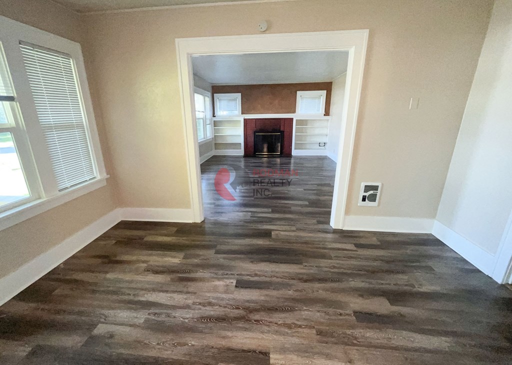 A room with a wooden floor and a fireplace in the background.