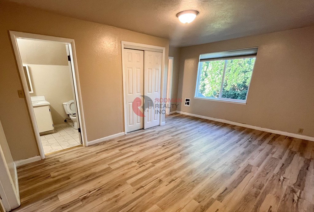 A room with wooden flooring and a window showing greenery outside.