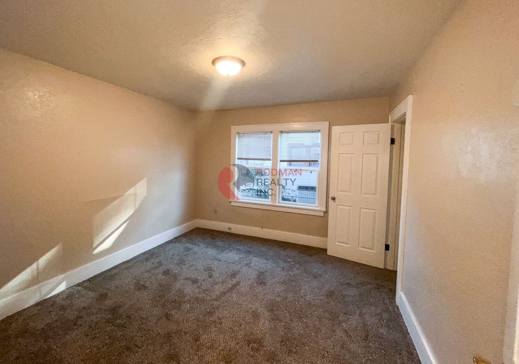 A room with a carpeted floor and a window showing a street view.