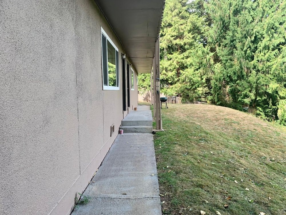 the side of a building with a sidewalk and trees
