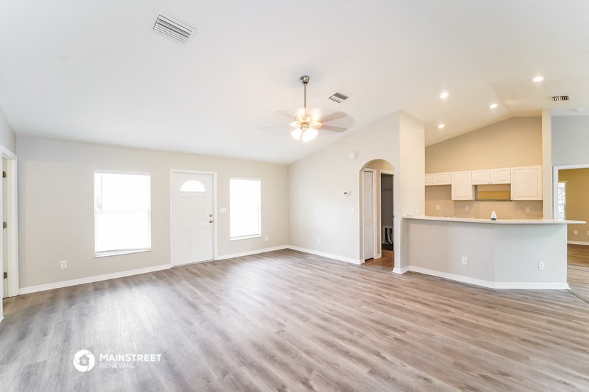 an empty living room with a kitchen and a ceiling fan