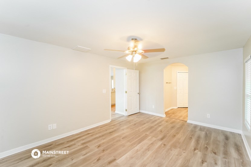a spacious living room with white walls and wood flooring and a ceiling fan