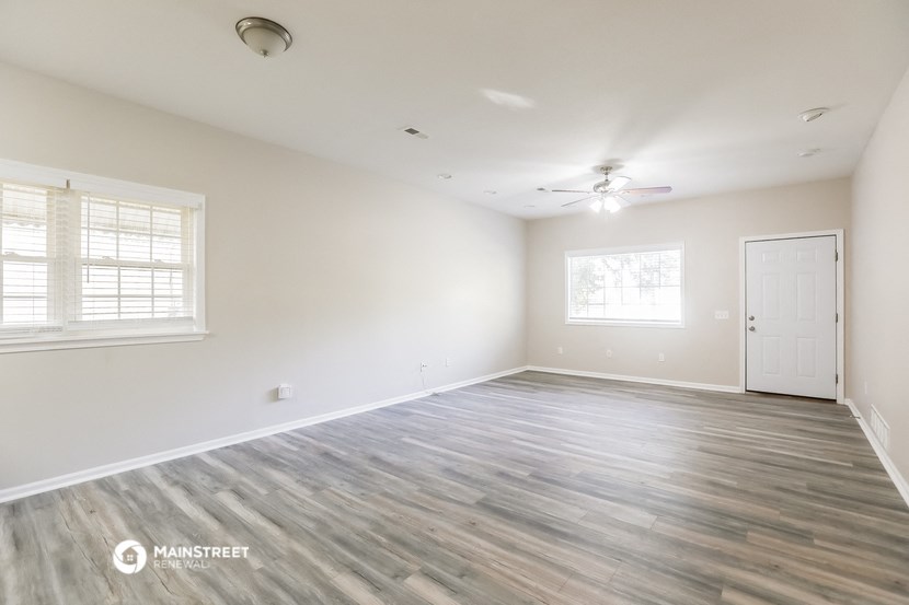 the spacious living room with white walls and a ceiling fan