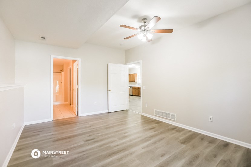 a spacious living room with white walls and wood flooring and a ceiling fan