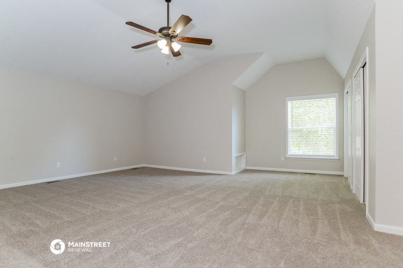 the spacious living room with ceiling fan and carpeting