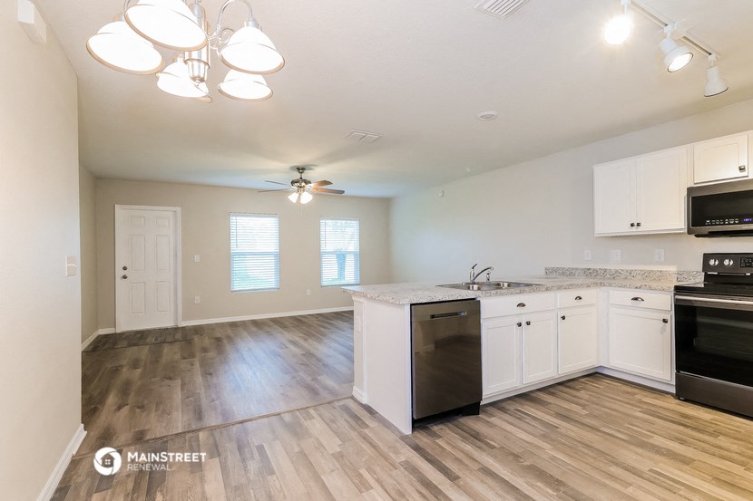 the kitchen and living room of an apartment with hardwood floors and white cabinets