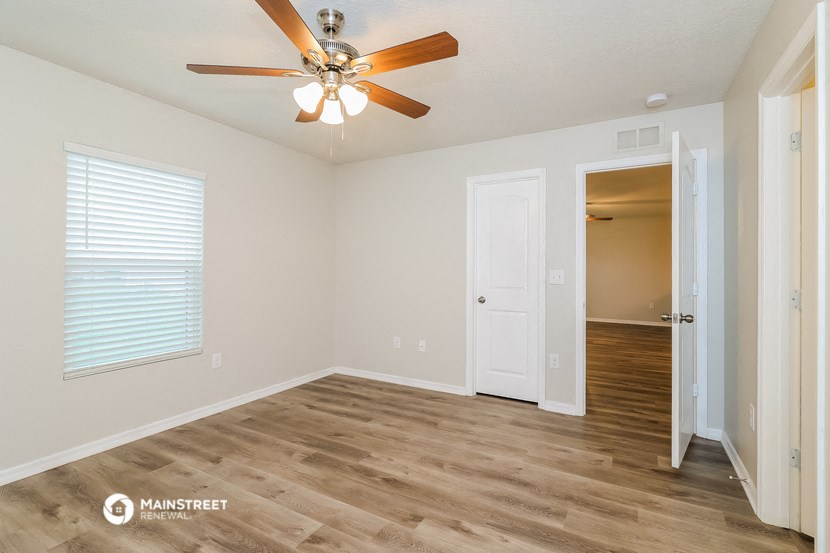the spacious living room with a ceiling fan and a door to the hallway